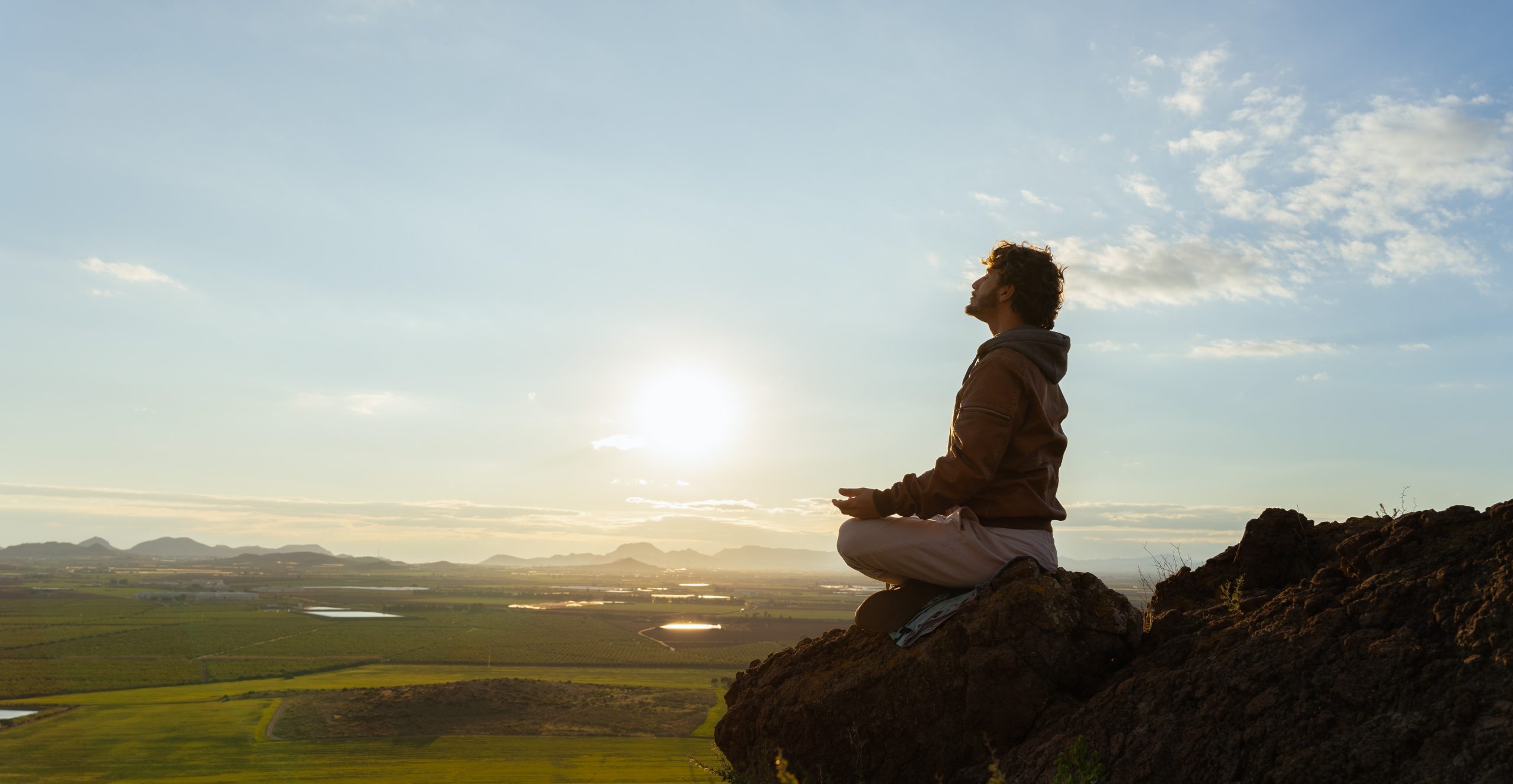 Homem sentado no cimo de uma montanha em pose meditativa a respirar para melhorar o seu bem-estar